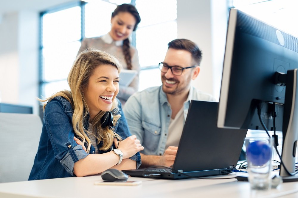 Group of office workers looking at a computer screen, conversing.