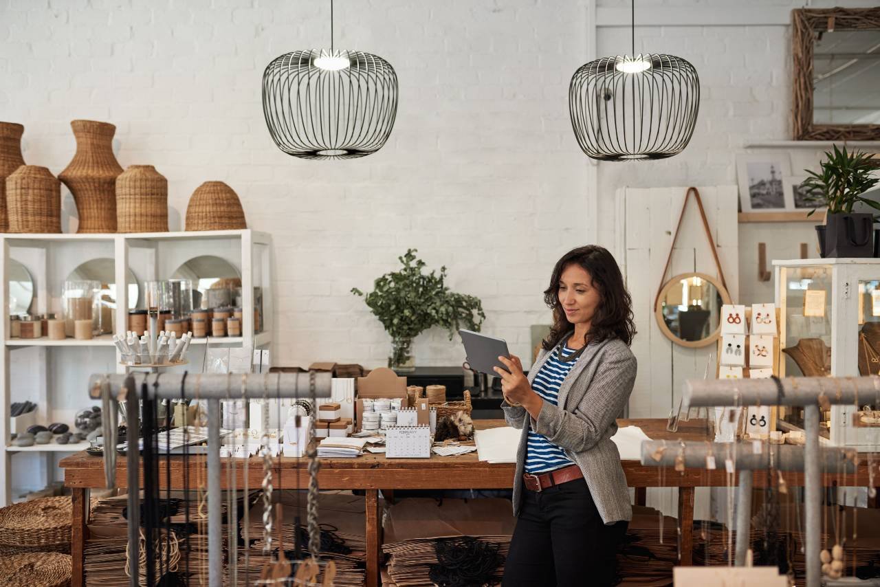 Image shows woman standing in a high-end retail outlet using a tablet computer to help manage the business.