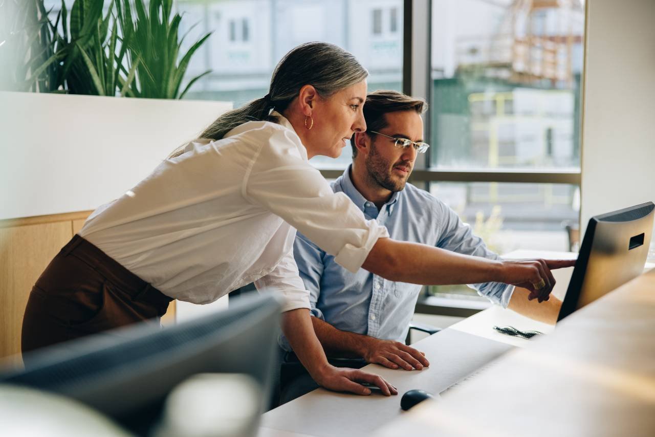 Image shows man and woman looking at a computer monitor with the woman pointing to something.